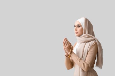 Young Muslim woman praying on light background. Islamic New Year celebration