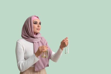 Young Muslim woman with lantern and prayer beads on green background. Islamic New Year celebration
