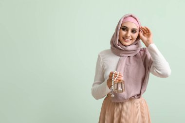 Young Muslim woman with lantern and prayer beads on green background. Islamic New Year celebration