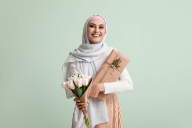 Young Muslim woman with flowers and gift on green background. Islamic New Year celebration