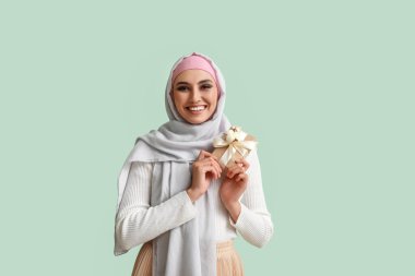 Young Muslim woman with gift on green background. Islamic New Year celebration