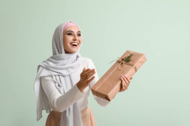 Young Muslim woman with gift on green background. Islamic New Year celebration