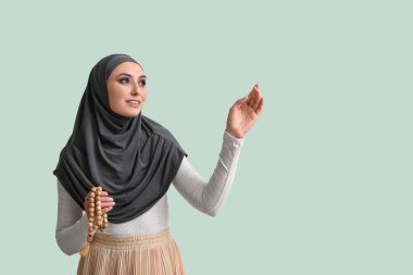 Young Muslim woman with prayer beads on green background. Islamic New Year celebration