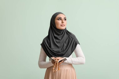 Young Muslim woman with Koran and prayer beads on green background. Islamic New Year celebration