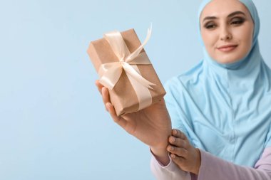 Young Muslim woman with gift on blue background, closeup. Islamic New Year celebration