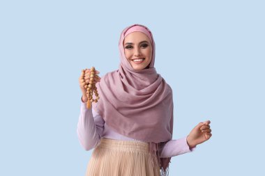 Young Muslim woman with prayer beads on blue background. Islamic New Year celebration