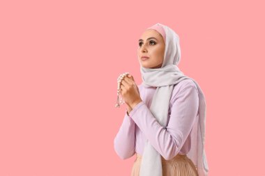 Young Muslim woman with prayer beads on pink background. Islamic New Year celebration