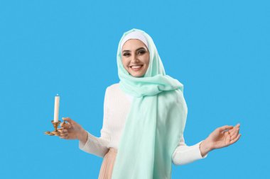 Young Muslim woman with burning candle on blue background. Islamic New Year celebration