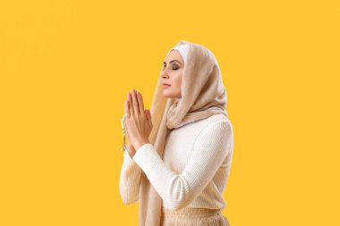 Young Muslim woman with prayer beads on yellow background. Islamic New Year celebration