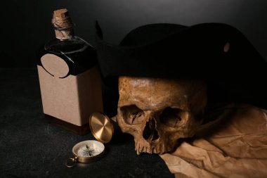 Pusulalı insan kafatası, siyah arka planda bir şişe rom ve korsan şapkası.