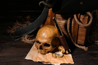 İnsan kafatası, kılıç, dürbün ve pusula kahverengi ahşap arka planda.