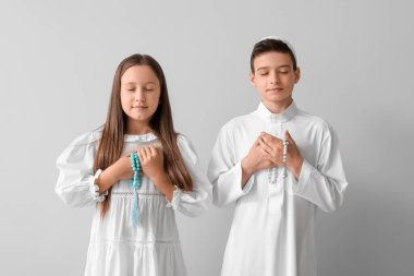 Little Muslim children with praying beads on light background