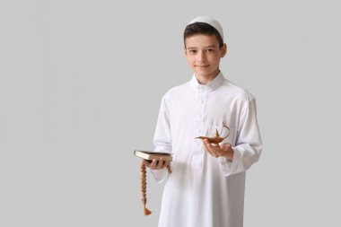 Little Muslim boy with Quran, Aladdin lamp and praying beads on light background