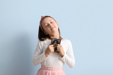Little Muslim girl with Quran on light blue background