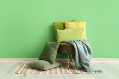 Ottoman with soft cushions near green wall