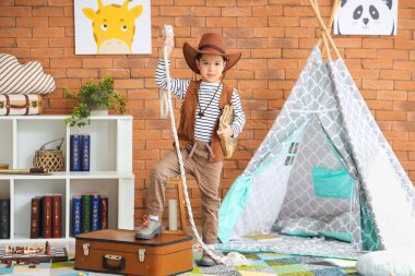 Cute little cowboy with adventure book and rope at home