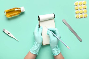 Doctor writing in notebook on mint background, top view