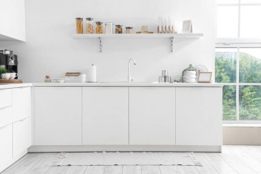 Modern mutfağın içinde lavabo ve çatal bıçaklarla dolu beyaz tezgahlar.