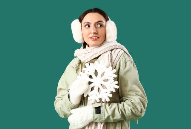 Yeşil arka planda kar taneleri olan kışlık elbiseli genç bir kadın.