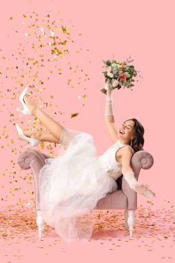 Beautiful bride with wedding bouquet in armchair and confetti on pink background