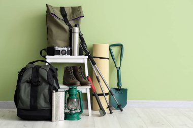 Set of camping equipment with backpack, oil lantern and outdoor gear near green wall