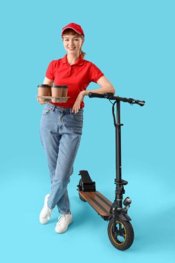 Portrait of female courier with takeaway coffee cups and kick scooter on blue background