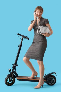 Portrait of young businesswoman with kick scooter and phone on blue background