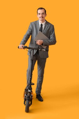 Handsome businessman with clipboard and kick scooter on yellow background