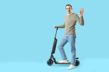 Young man with kick scooter on blue background
