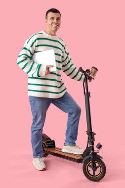 Young man with laptop and kick scooter on pink background