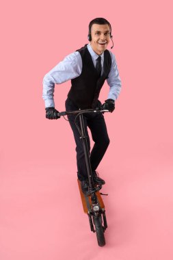 Male worker in headset with kick scooter on pink background