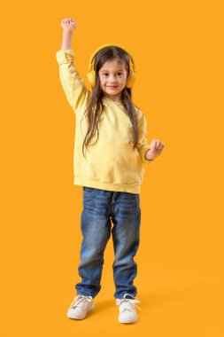 Cute little girl in headphones dancing on yellow background