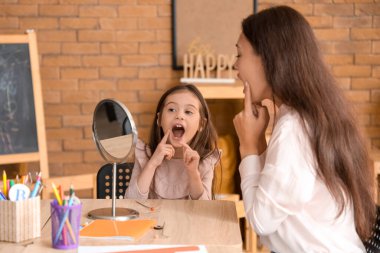 Female Asian speech therapist working with little girl at table in office