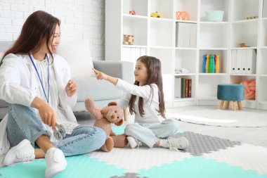 Female Asian speech therapist showing letter to little girl in office