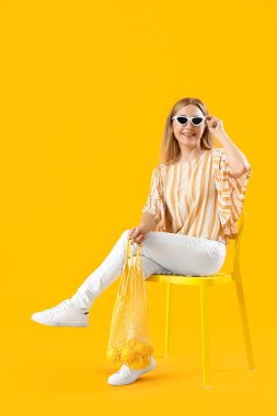 Mature woman with string bag of lemons sitting in chair on yellow background