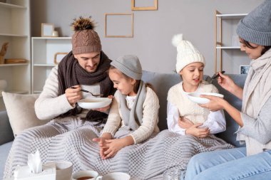 Ill little girls with their parents eating soup at home