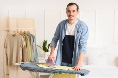 Young man ironing t-shirt on board in laundry room