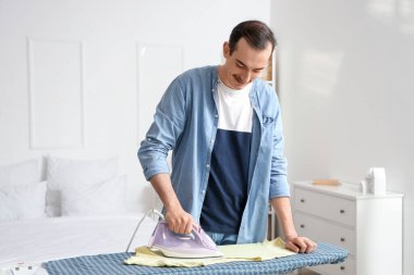 Young man ironing t-shirt on board in laundry room