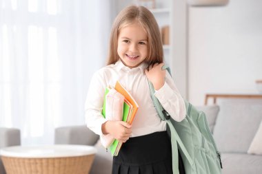 Cute little schoolgirl with backpack and copybooks at home