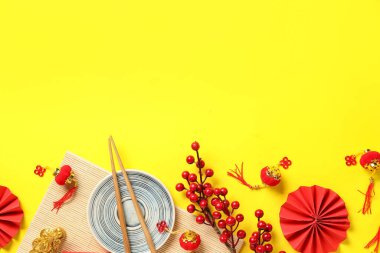 Bamboo mat with plate, chopsticks and decor on yellow background. Chinese table setting