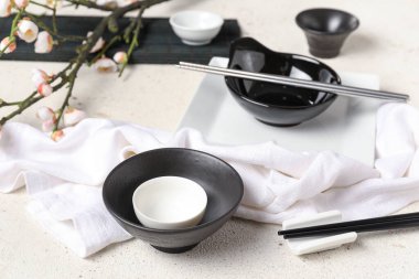 Bowls with cups, chopsticks and sakura branch on white grunge background. Chinese table setting