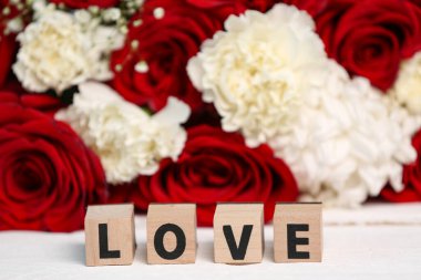 Beautiful flowers and word LOVE made of cubes on white wooden table