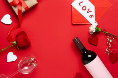Frame made of bottle with wine, flowers, glass and hearts on red background. Valentine's Day celebration