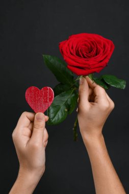 Female hands with beautiful red rose and heart on black background