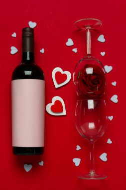 Bottle of wine with glasses and rose on red background. Valentine's Day celebration