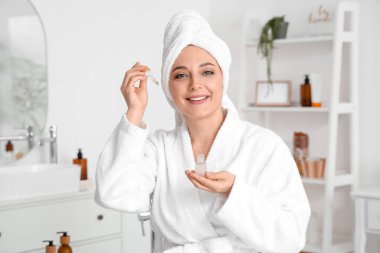 Mature woman applying serum after shower in bathroom