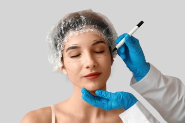 Plastic surgeon marking woman's face on light background, closeup