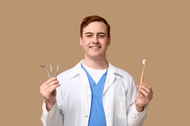 Male dentist with dental tools and toothbrush on beige background. World Dentist Day