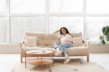 Young African-American woman sitting on sofa at home