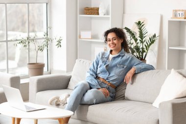 Young African-American woman sitting on sofa at home